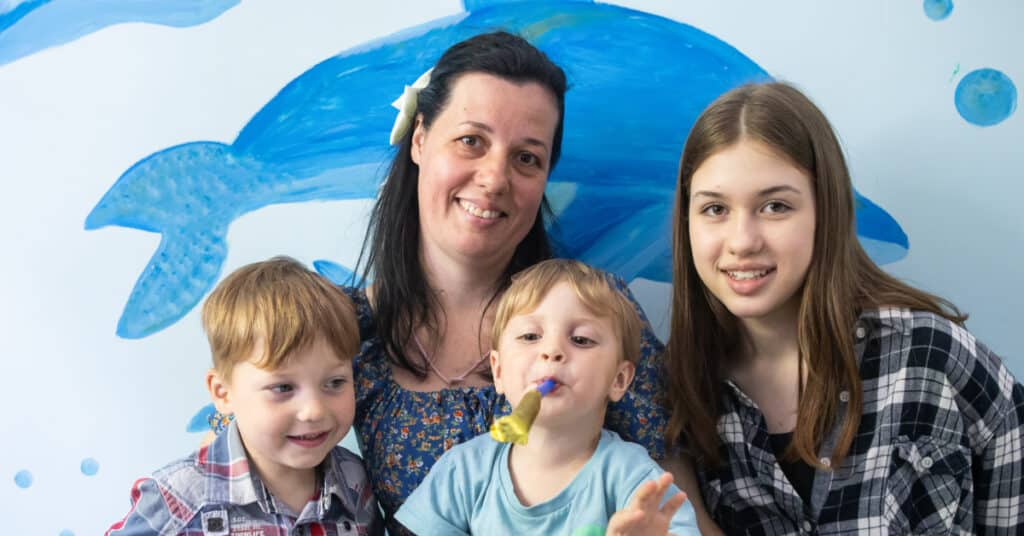 Olga, a woman with long brown hair, sits with three of her children – two young boys, and one teenage girl.