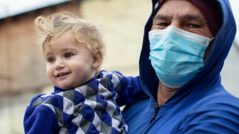 The father holds his youngest daughter outside with mask on