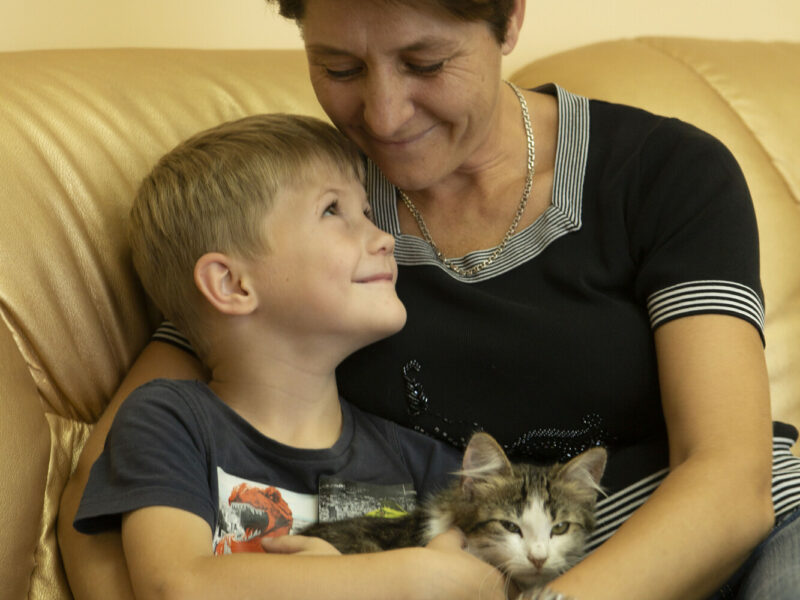 A mother holds her young son in a hug on the sofa as they smile at one another