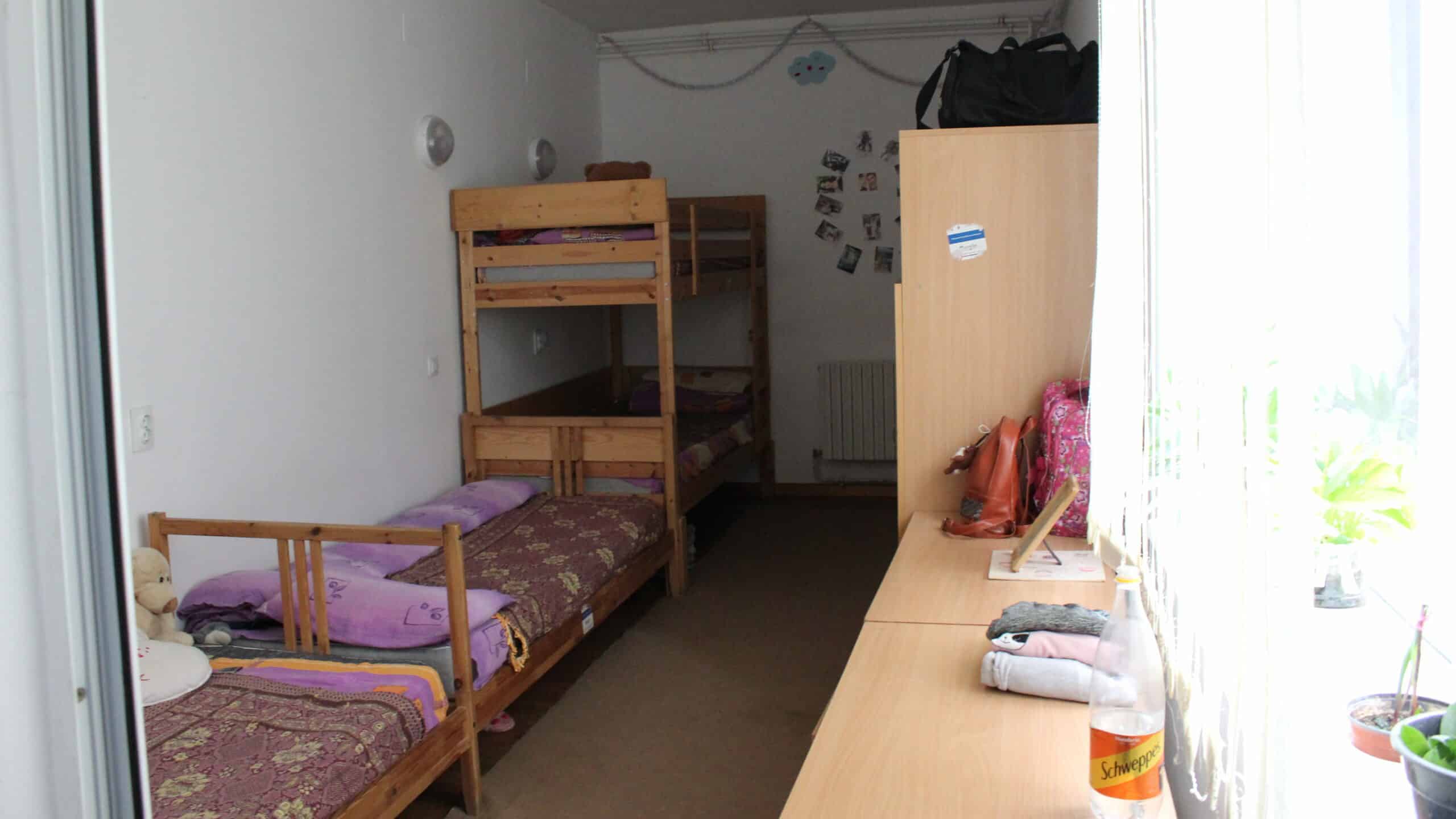 A child's bedroom inside the orphanage, with three beds squished together in cramped, dark conditions.