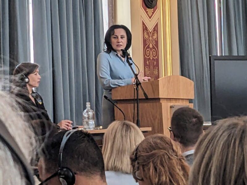 Ukrainian Minister Oksana Zholnovych stands at a podium in a grand ballroom at the Foreign Commonwealth and Development Office