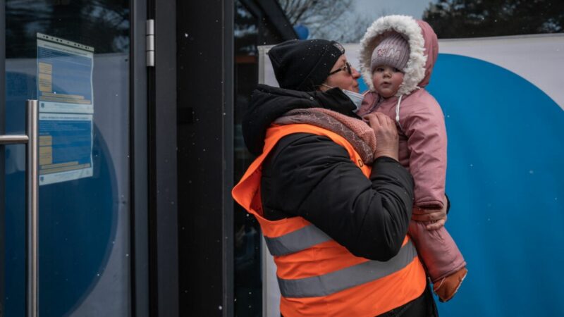 Scenes from the border between Romania and Ukraine during the crisis. A child is being held by a man in a high visibility vest while it snows.