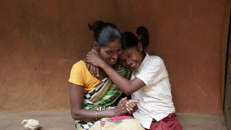 A young teenage girl, Sonia, hugs her mother outside their family home in rural India