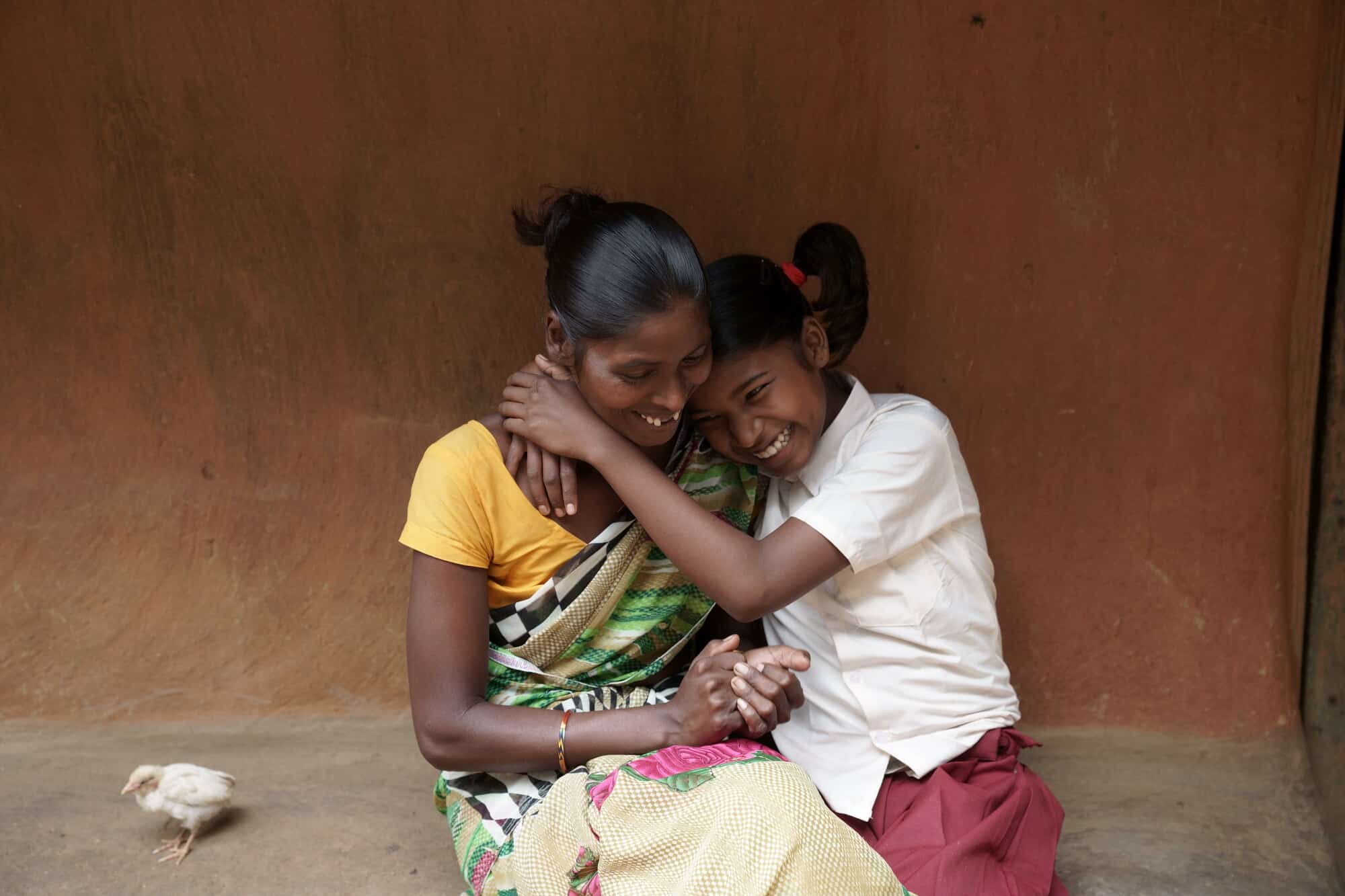 A young teenage girl, Sonia, hugs her mother outside their family home in rural India