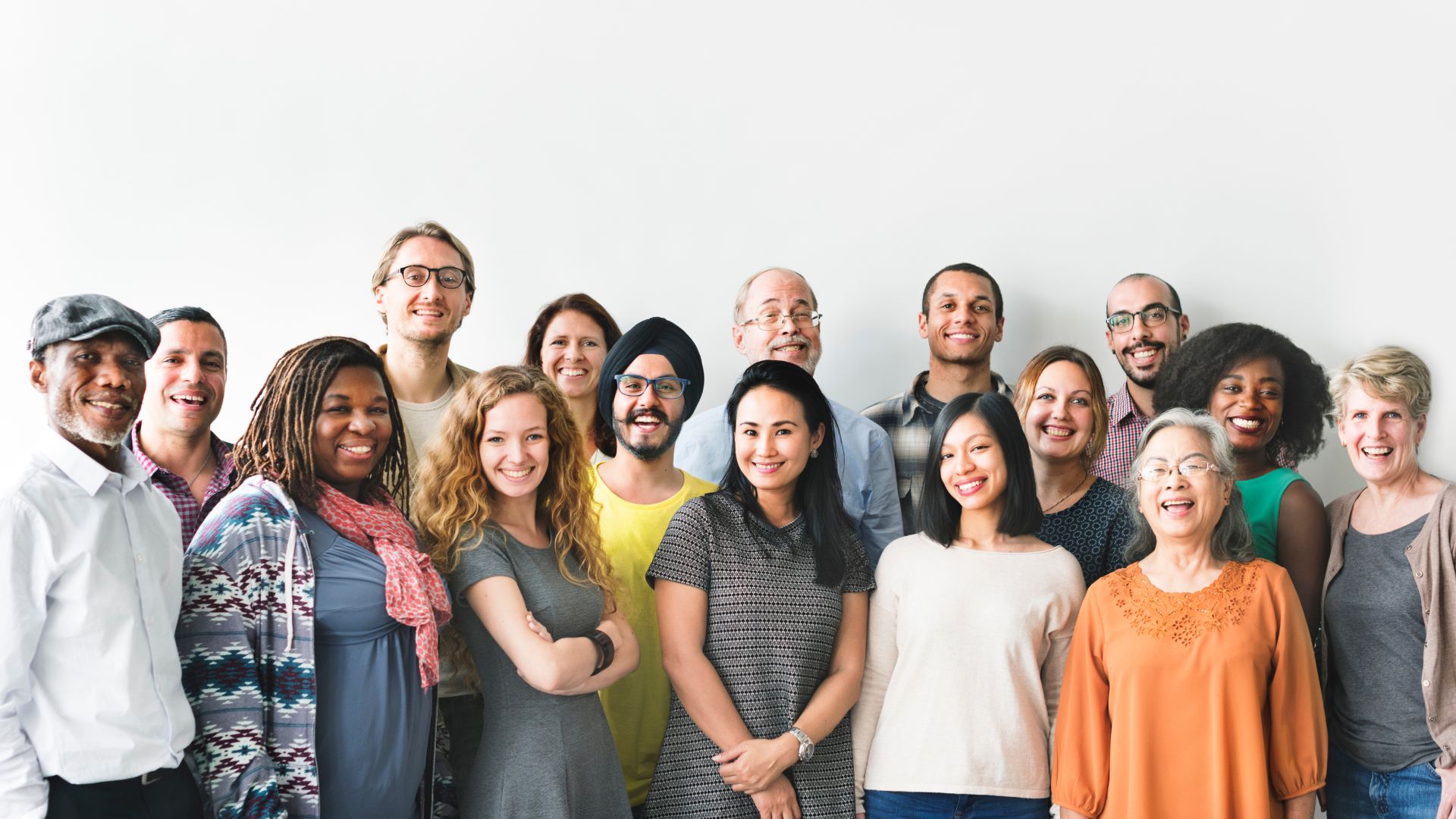 A diverse group of people standing together against a blank wall, smiling