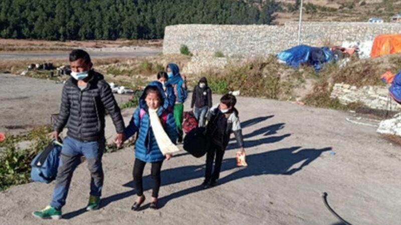 Nepali man leads 4 warmly dressed children across some tarmac outside a landing strip
