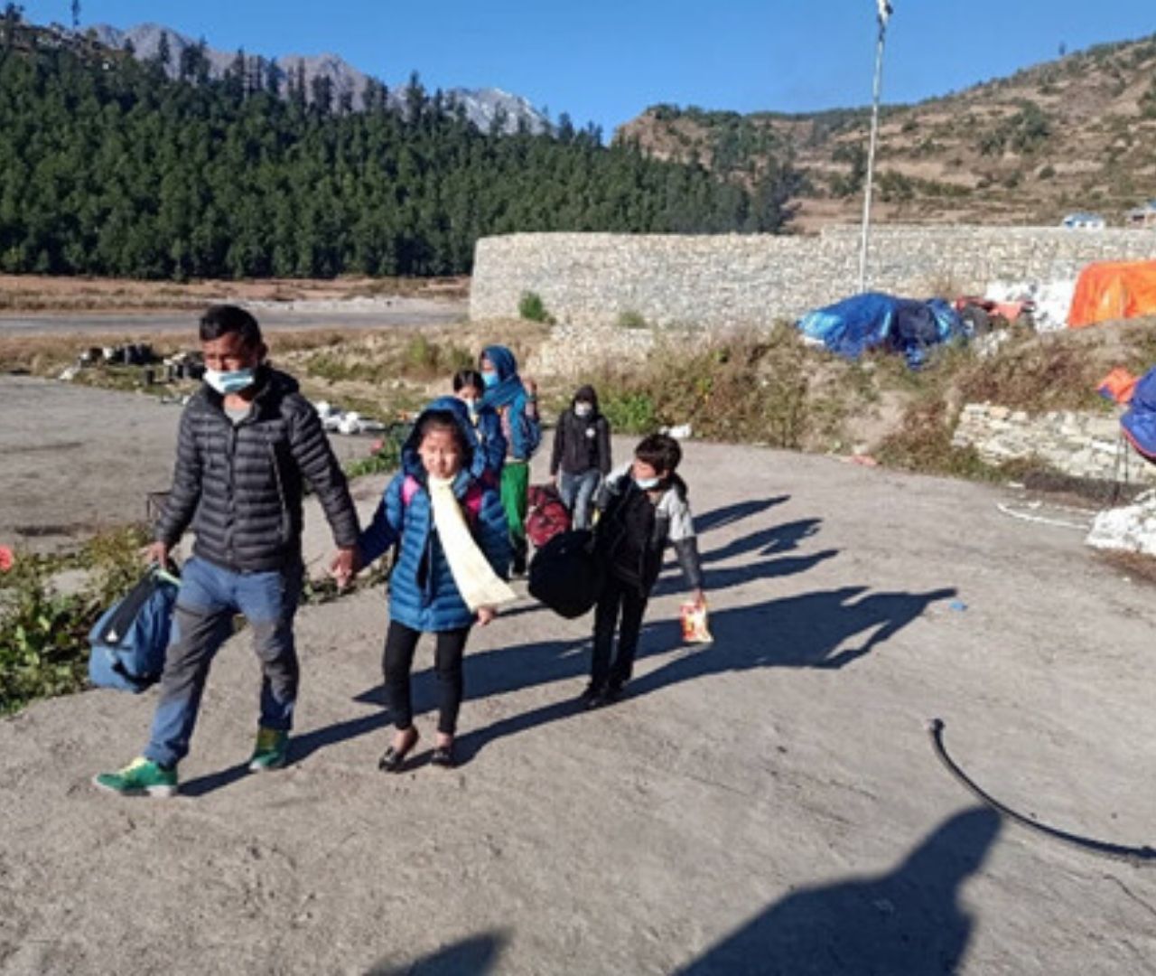 Nepali man leads 4 warmly dressed children across some tarmac outside a landing strip