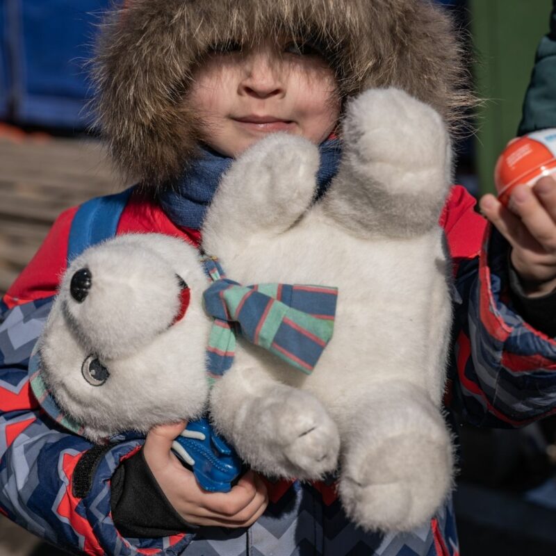 A child carrying a teddy bear, holding their parent's hand,